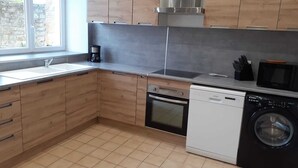 Una cocina moderna con armarios de madera, una campana extractora de acero inoxidable, lavavajillas, lavadora y microondas.