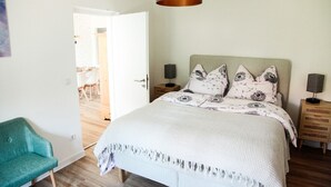 Une chambre à coucher comprenant un lit, des tables de chevet, une lampe, une chaise et une porte donnant sur une autre pièce.