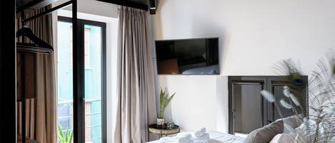 Un dormitorio con cama, televisor, armario, planta y balcón.