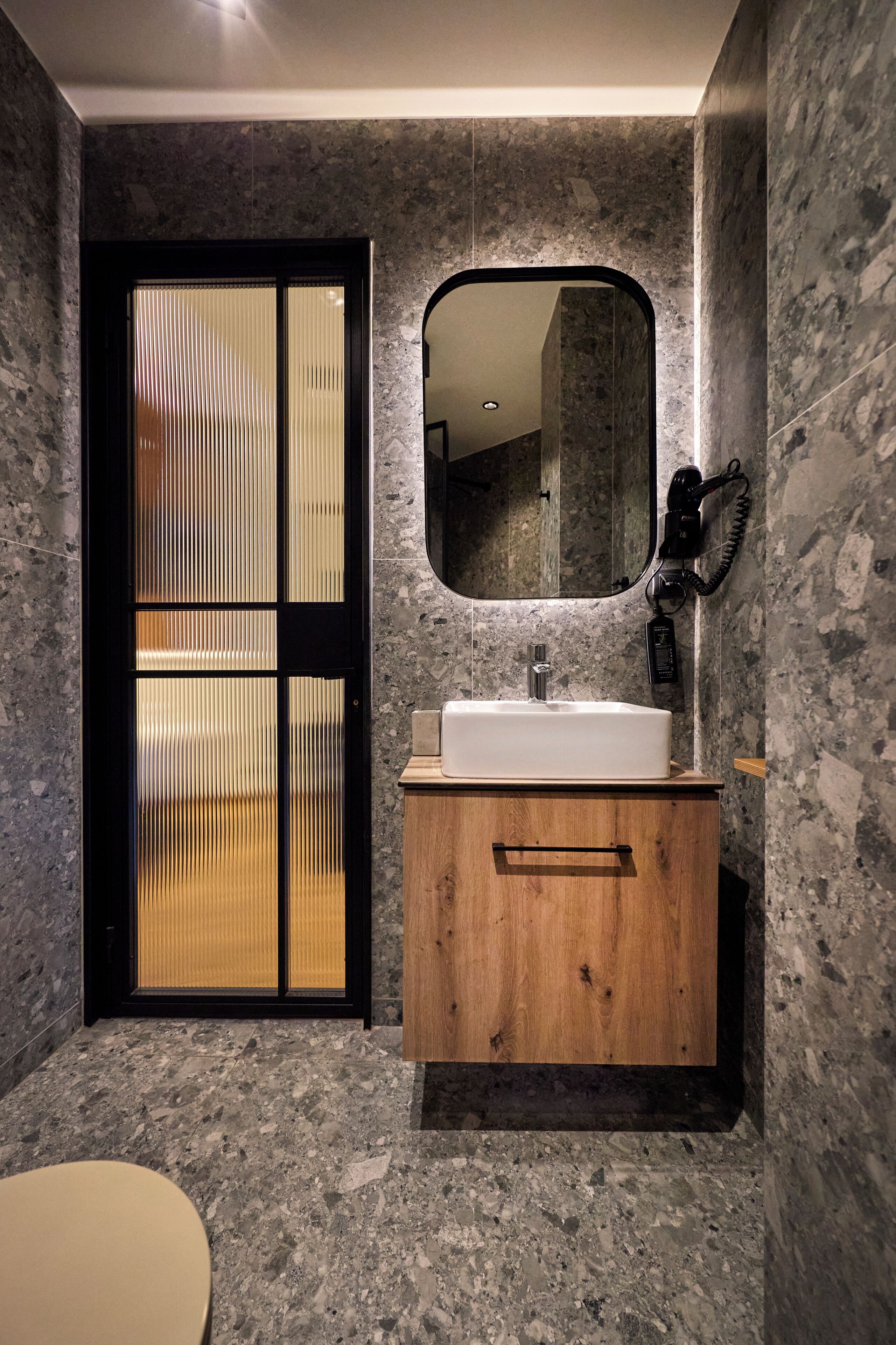 A bathroom with a wooden vanity, a white sink, a mirror, and a hairdryer on the wall.