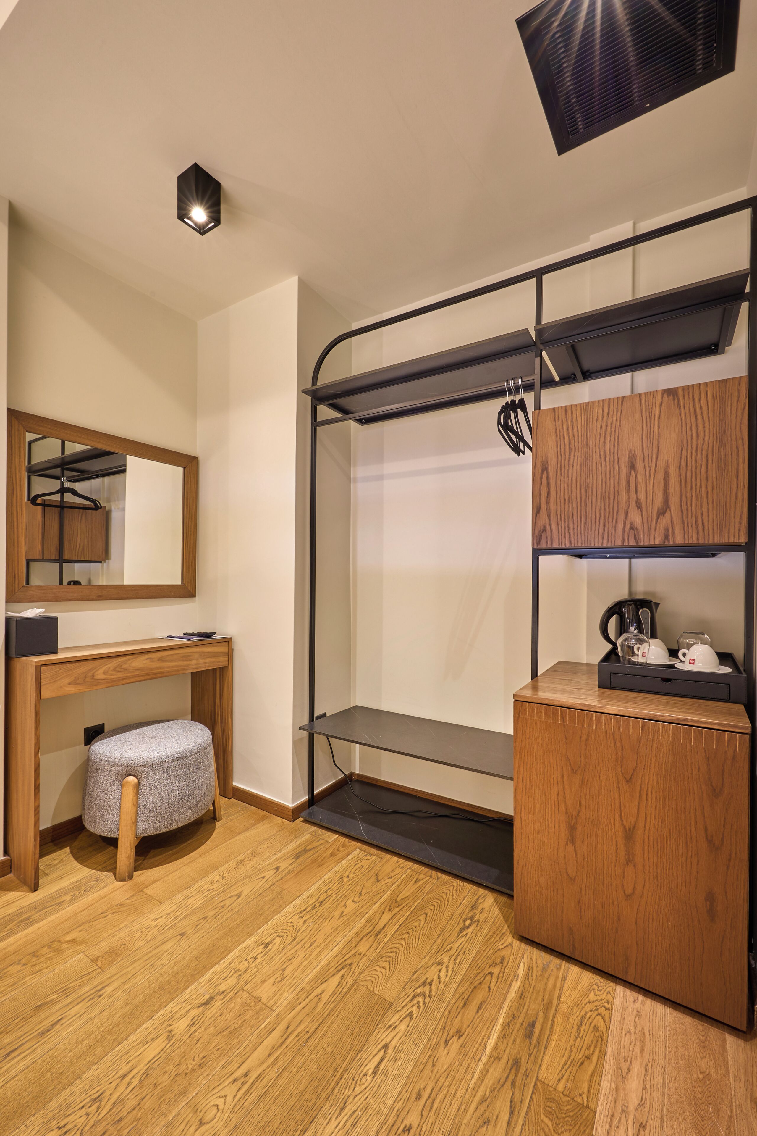 Habitación pequeña con suelo de madera, un banco, un espejo, un estante con un hervidor y un perchero.