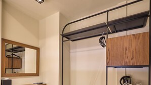 Une petite pièce avec un plancher en bois, un banc, un miroir, une étagère avec une bouilloire et un porte-manteau suspendu.