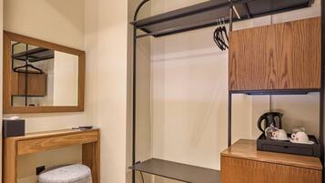 Habitación pequeña con suelo de madera, un banco, un espejo, un estante con un hervidor y un perchero.