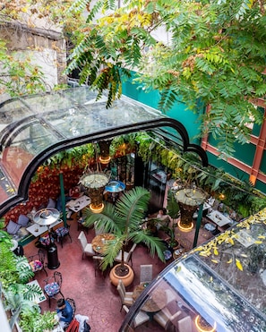 An indoor garden with tables and chairs, surrounded by lush greenery and hanging plants. - Mamy Blue Slow Living (Athens)