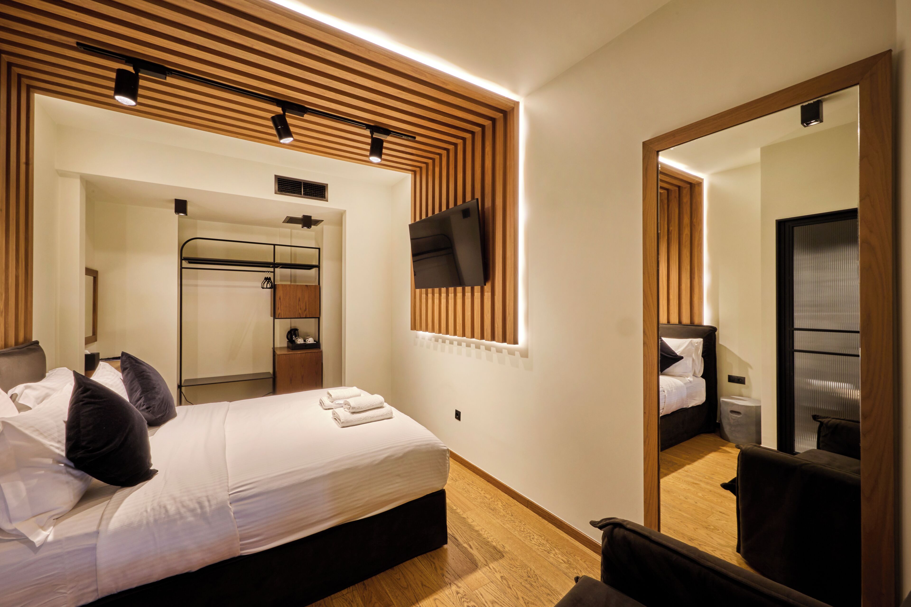 A modern hotel room with a large bed, a wardrobe, a mirror, and a flat-screen TV mounted on the wall.