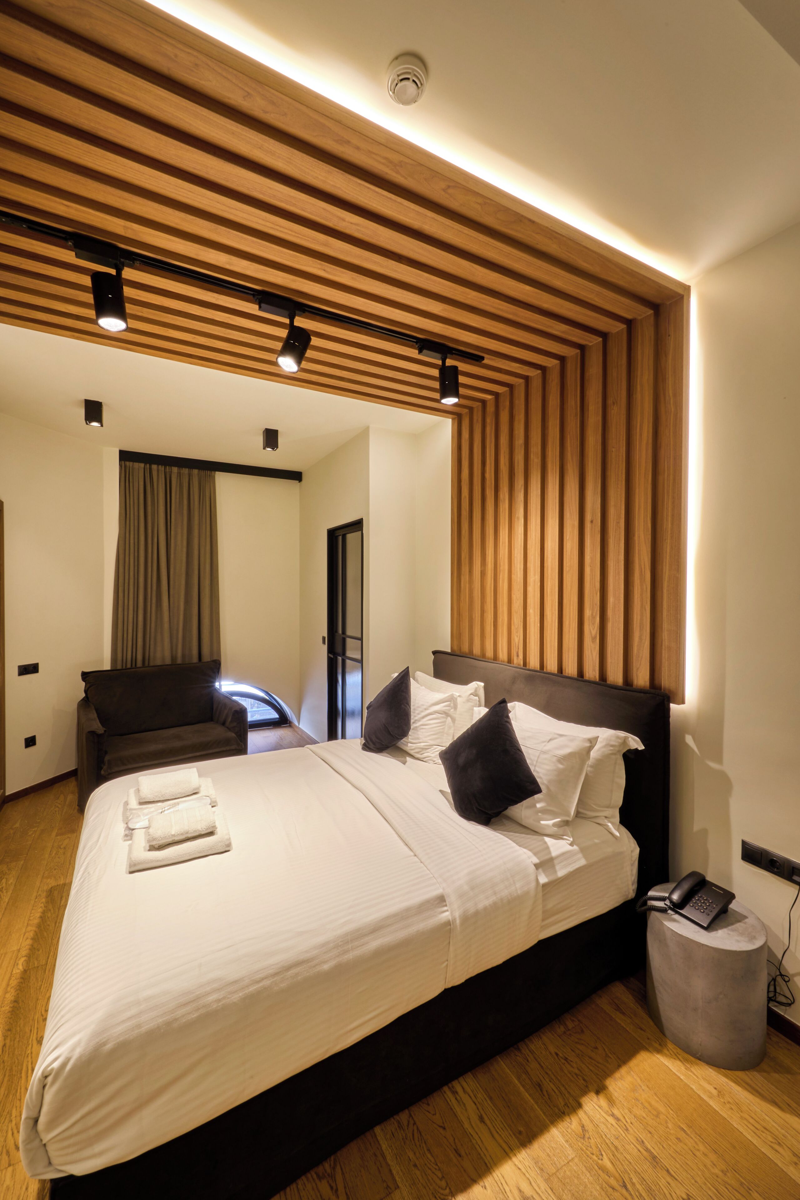 Une chambre d’hôtel moderne avec un plafond en bois, un grand lit avec du linge de lit blanc, une table de chevet avec un téléphone et une chaise.