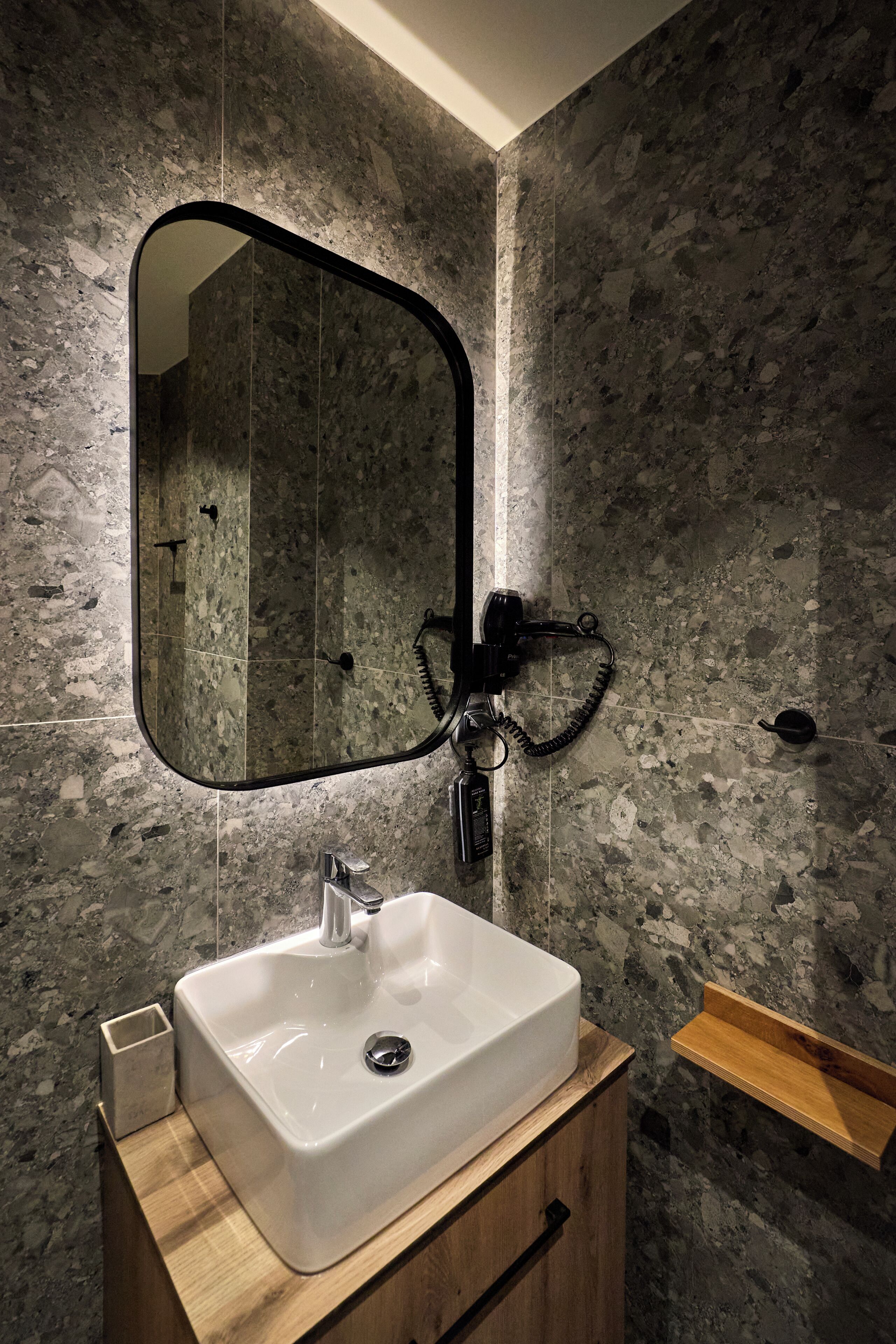 A bathroom with a white sink, a wooden vanity, a black-framed mirror, and a marble wall.