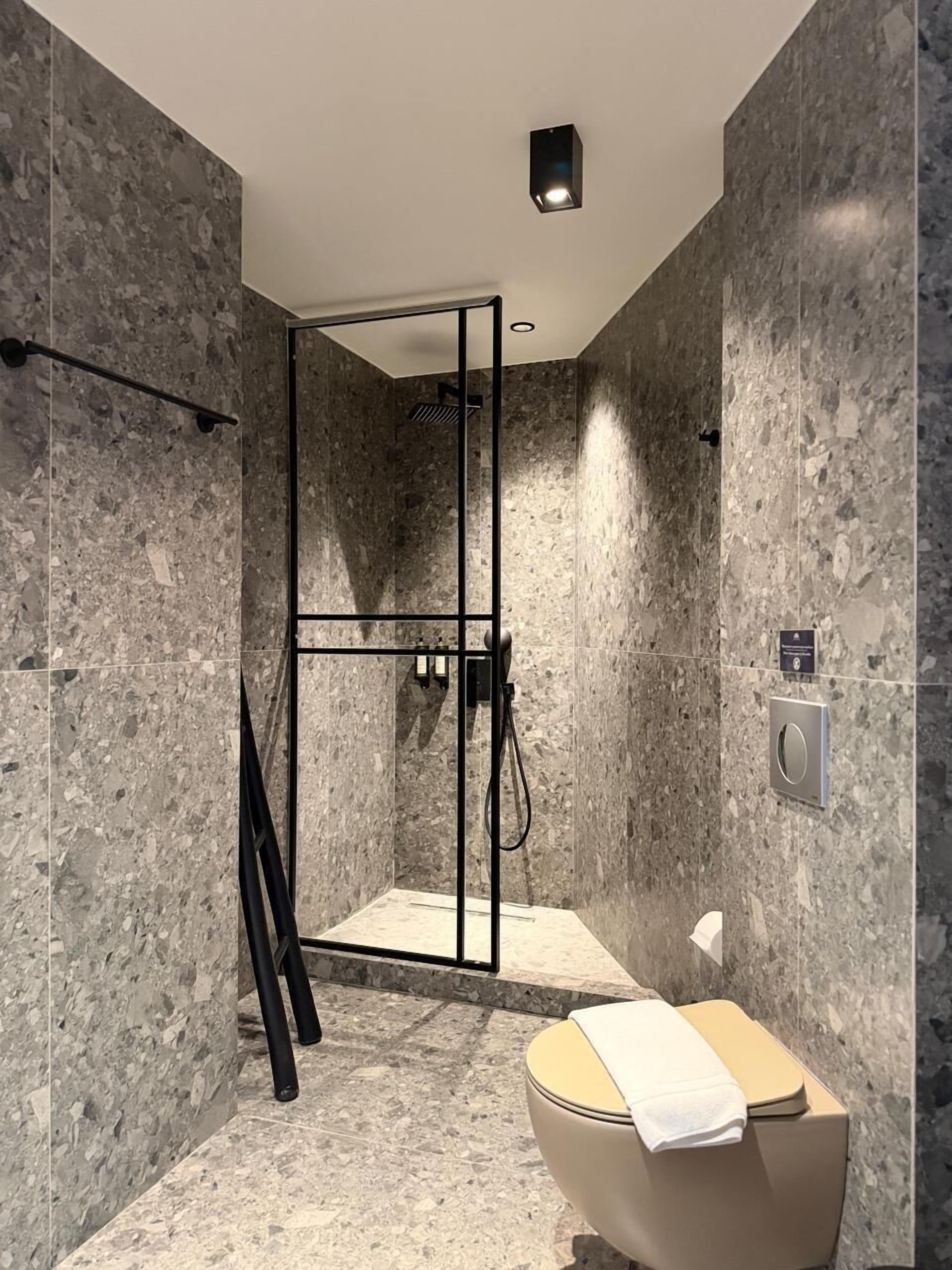 A modern bathroom with a glass-enclosed shower, a toilet, and a marble wall.
