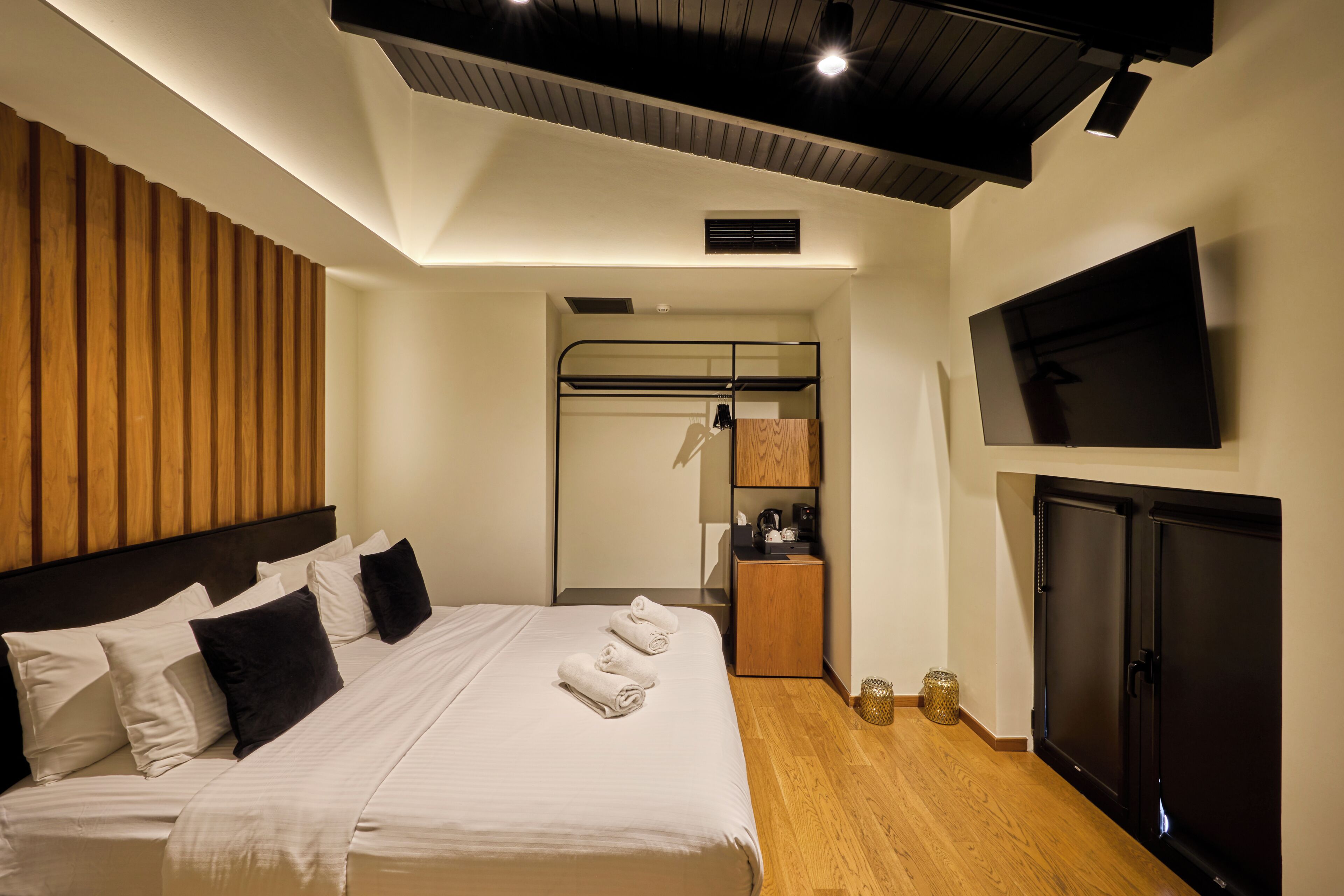 A modern hotel room with a bed, a TV, a wardrobe, and a small kitchenette.