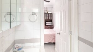 A modern bathroom with a white sink, a mirror, and a door leading to a bedroom.