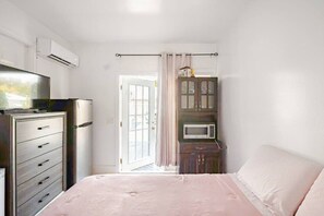 A bedroom with a bed, a dresser, a microwave, and a door leading to a balcony. - Room in Guest Room - Small Studio Apartment (Vero Beach)