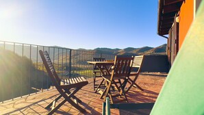 Ein Balkon mit Tisch und Stühlen mit Blick auf eine gebirgige Landschaft.