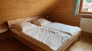 A wooden cabin bedroom with two beds, a nightstand, and a window with curtains. - Come and Find This House for Holidays (Oberharz am Brocken)