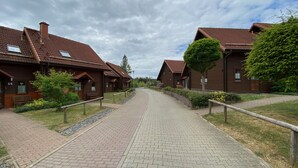Ein Weg zu Holzhäusern mit roten Ziegeldächern, Bänken und viel Grün.