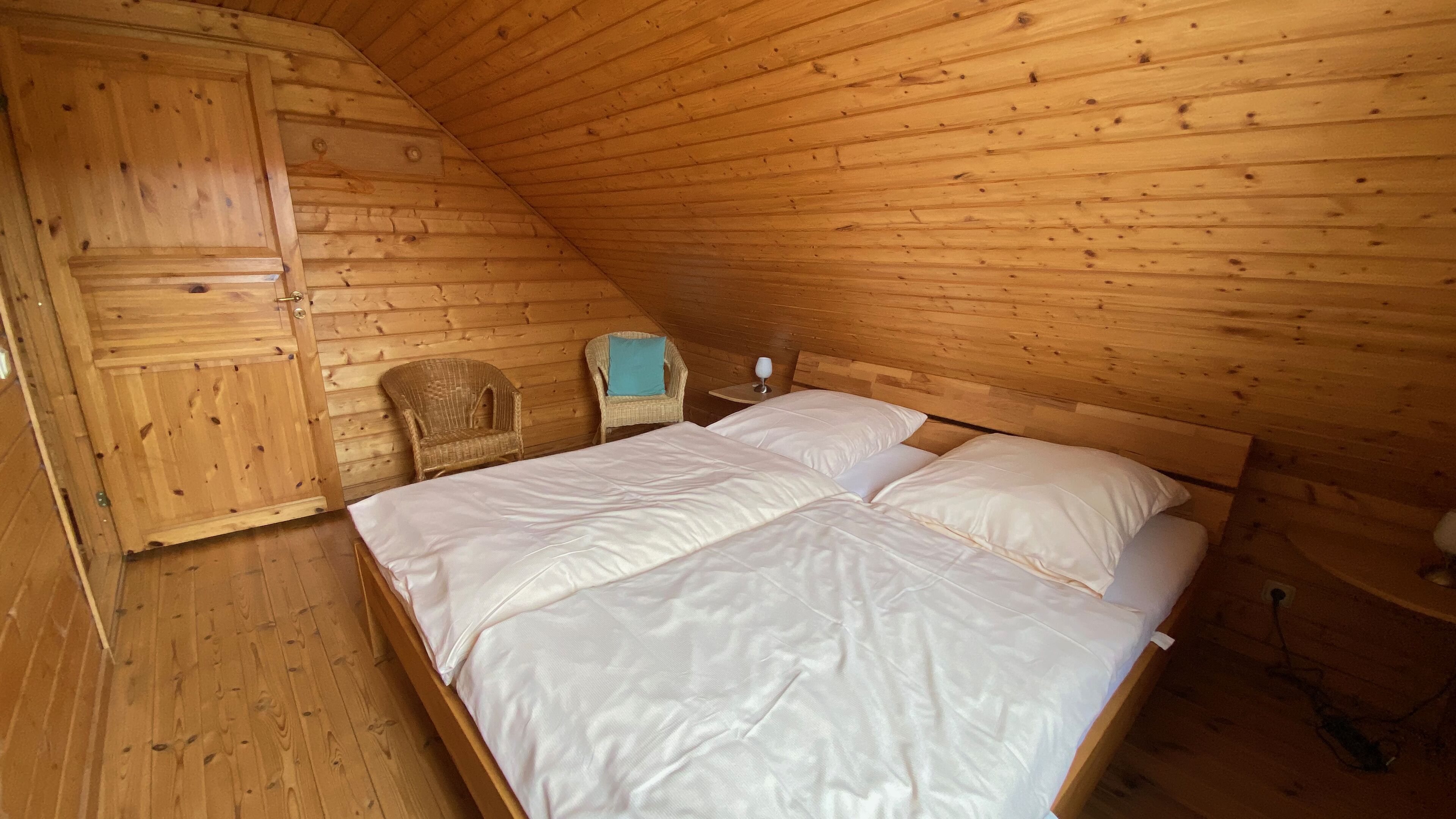 A wooden cabin bedroom with a bunk bed, a wicker chair, and a small table with a glass.