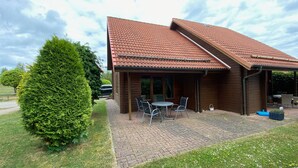 Eine Holzhütte mit einem Ziegeldach, einer Terrasse mit Stühlen und einem großen Baum in der Nähe.