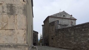 A narrow cobblestone street with historic stone buildings, one with a visible window and a small balcony. - Casa Moratto in the Heart of Buje (Buje)