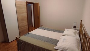 A bedroom with a bed, wooden floor, white walls, a door, and a bedside table with a lamp. - Casa Moratto in the Heart of Buje (Buje)