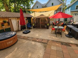 Un patio trasero con un jacuzzi inflable Coleman, una zona de estar cubierta y un paraguas rojo.