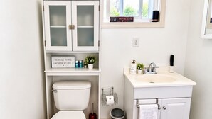 A bathroom with a toilet, a sink, a cabinet with glass doors, a trash can, and a blue rug. - Room-fall Room 3min From Yale, And Other (New Haven)