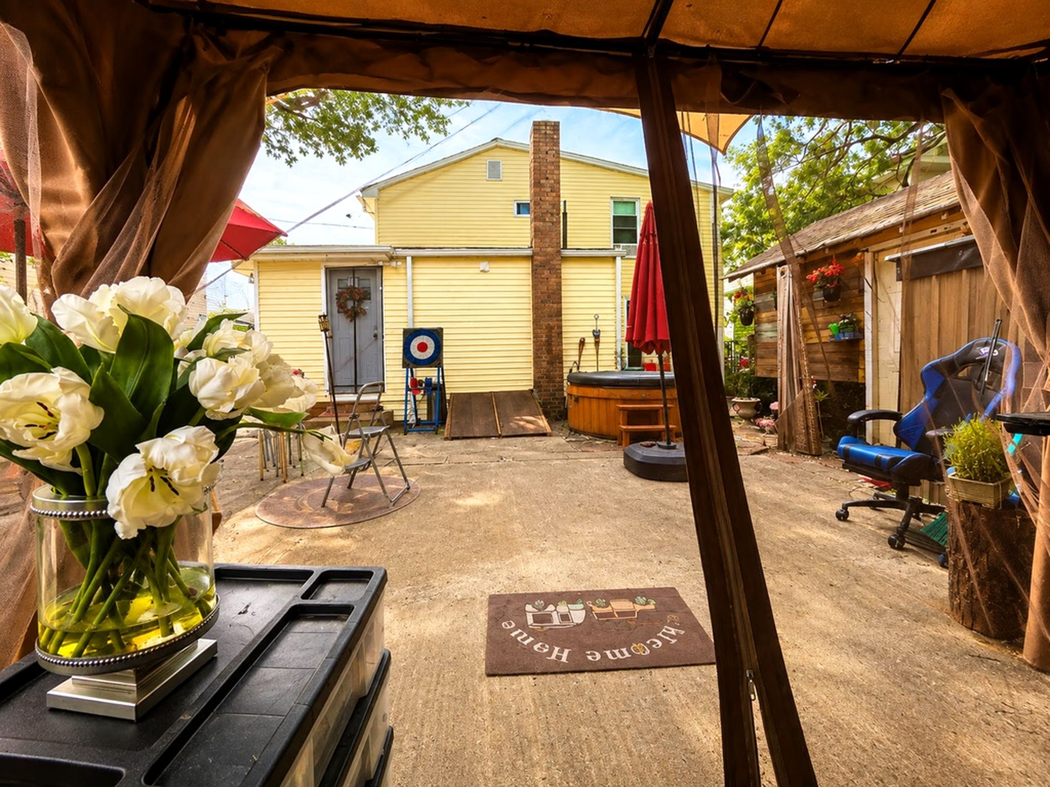 A covered outdoor area with a yellow building in the background, a target on the wall, and a welcome mat on the ground.