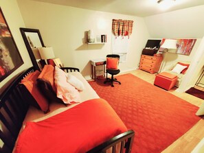 Ein Schlafzimmer mit einem Bett, einem Schreibtisch, einem Stuhl, einer Kommode und einem Fenster mit Vorhängen.