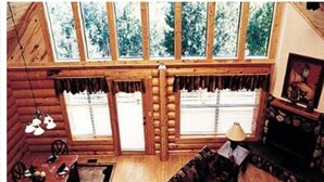 A log cabin interior with a large window, wooden walls, and a fireplace. - Entire Charming Cabin With Lake And Mountain View at Angel Fire (Angel Fire)