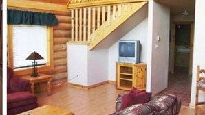 Ein rustikales Blockhaus-Interieur mit einer Holztreppe, einem Fernseher auf einem Holzständer und einem roten Sofa.