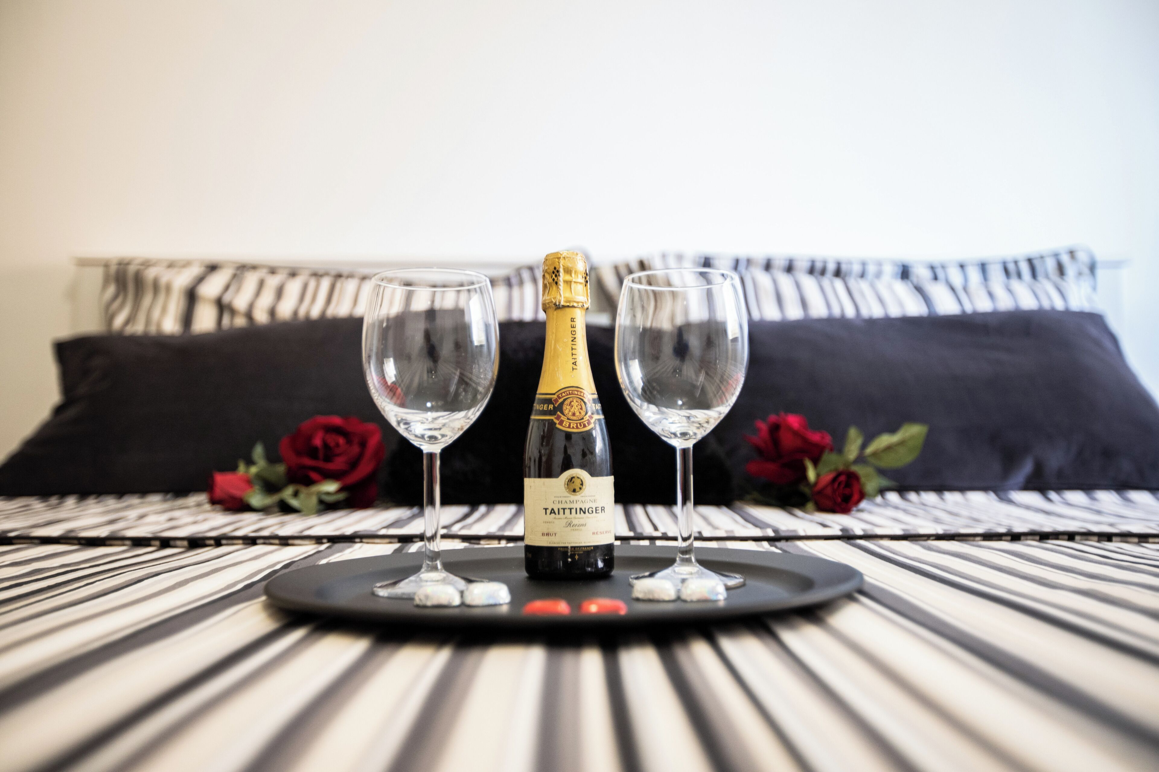 A bottle of Taittinger champagne on a tray with two glasses and rose petals on a striped table.