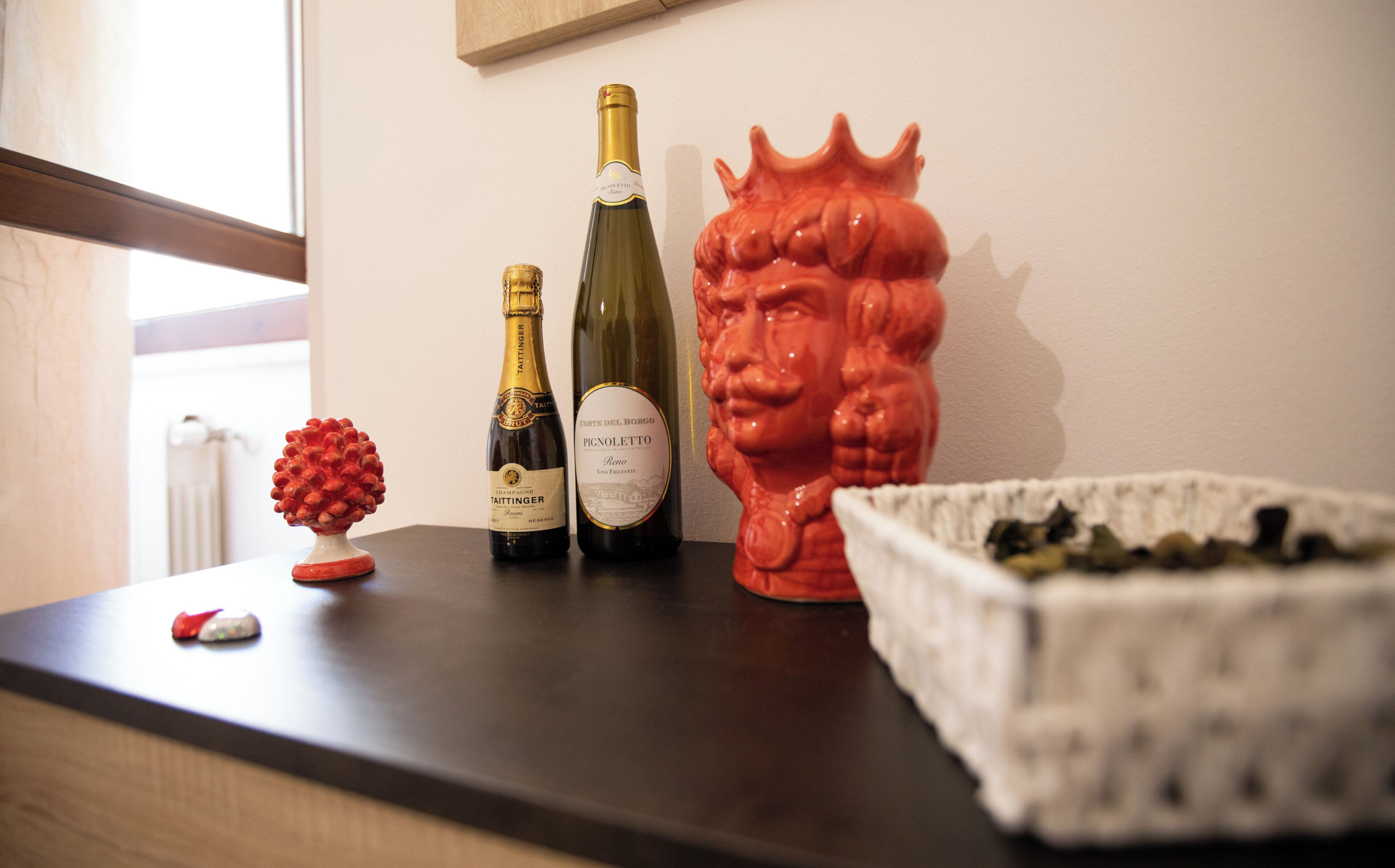 A wooden table with two bottles of wine, a decorative red sculpture, and a small red object.
