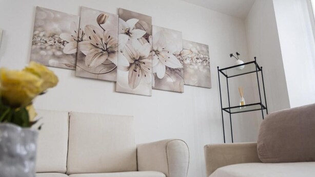 Een woonkamer met een beige bank, een salontafel en een zwart wandplankje met een vaas.