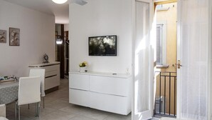 Een moderne keuken met witte kasten, een eethoek met een witte tafel en stoelen, en een aan de muur bevestigde televisie.