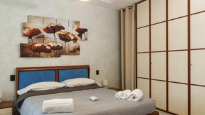 Een slaapkamer met een bed, nachtkastje, wanddecoratie en een schuifdeurkast.