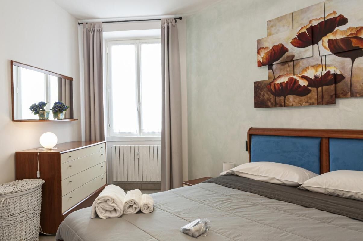 A hotel room with a bed, a dresser, a mirror, and a window with curtains.