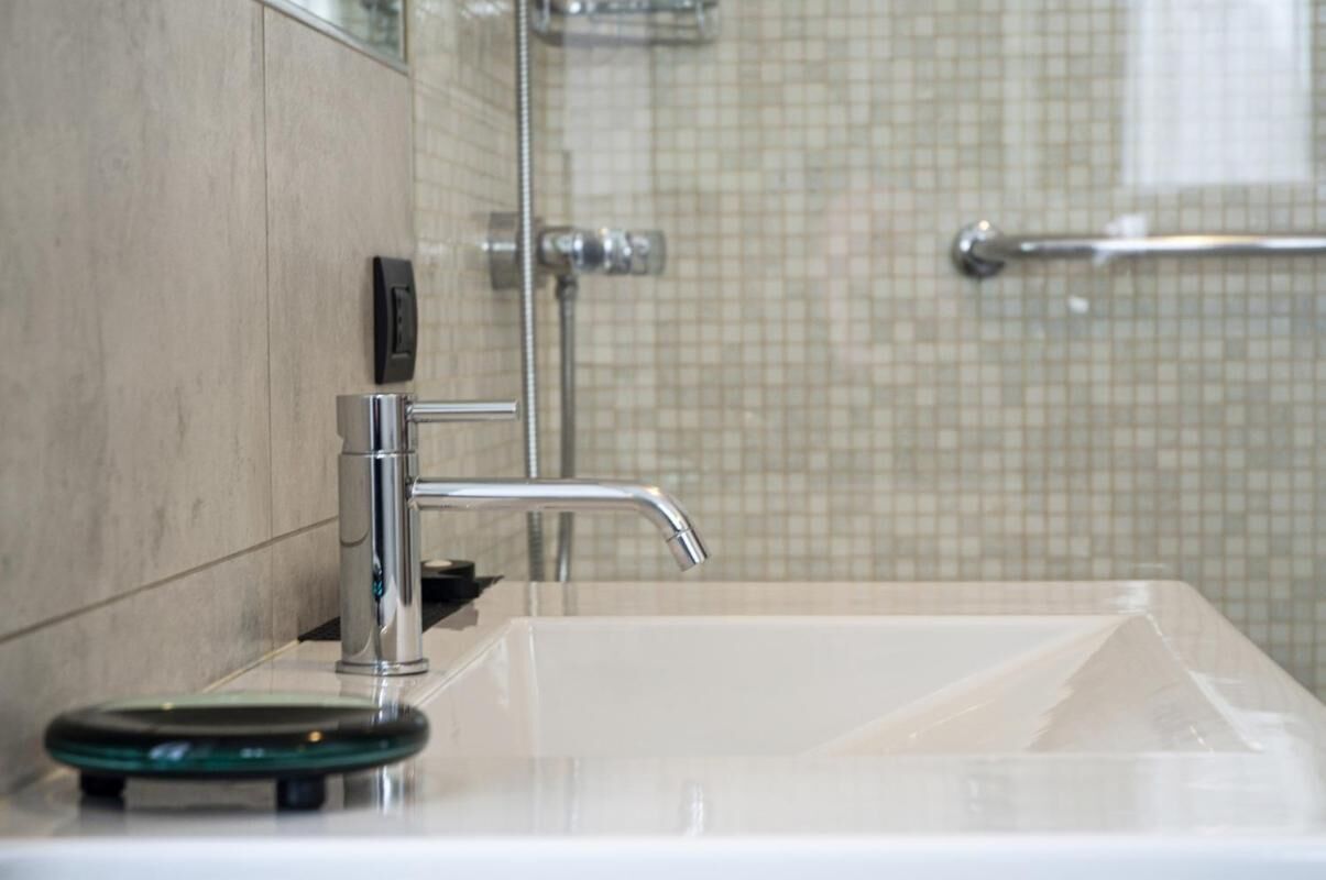 A bathroom with a white sink, chrome faucet, and a glass soap dish.