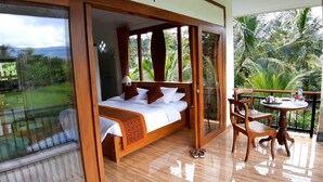 A bedroom with a bed, a balcony with a table and chairs, and a view of greenery. - Room-the Champuhan Villa - Honeymoon Vil (Seririt)