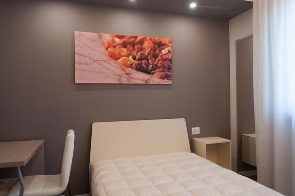 A hotel room with a bed, a chair, a small table, and a wall-mounted artwork.