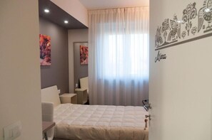 A bedroom with a bed, a desk, a chair, and a window with curtains.
