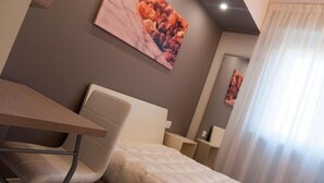Une chambre d’hôtel moderne, équipée d’un lit, d’un bureau et d’une chaise. Un tableau orne le mur, et une fenêtre est agrémentée de rideaux.