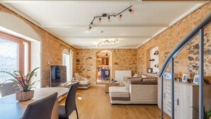 Un vaste espace de vie comprenant une table à manger en bois, des sièges confortables, une cuisine à l’arrière-plan et un mur en pierre.