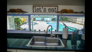 A kitchen with a view of a swimming pool, a stainless steel sink, and a 'let's eat' sign above the window. - Family Home With Private Pool & Yard Only 24 Mi to Disney (St. Cloud)