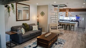 A modern living room with a grey sofa, a wooden coffee table, and a kitchen in the background. - Family Home With Private Pool & Yard Only 24 Mi to Disney (St. Cloud)