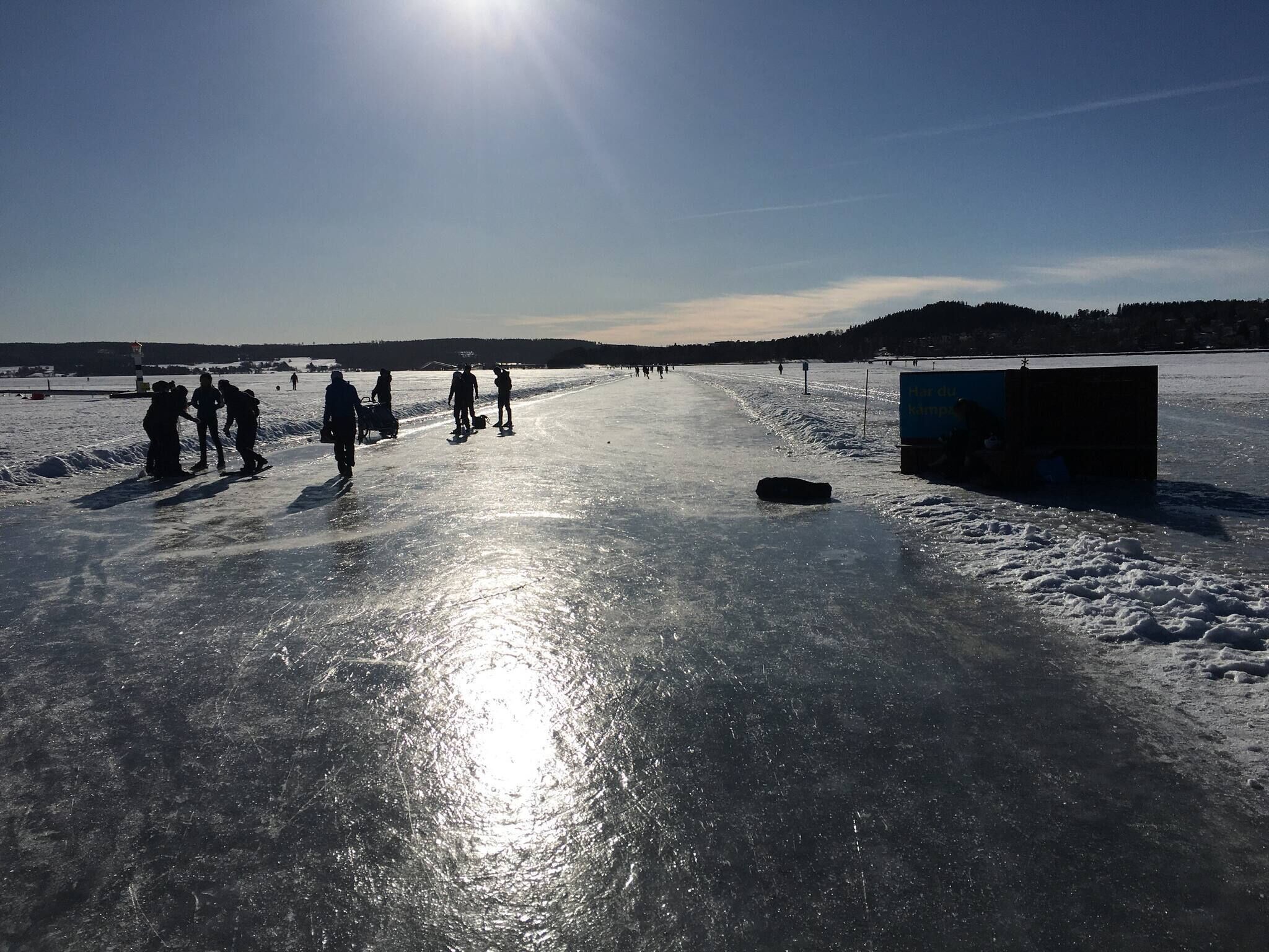 A frozen lake with people walking and a small structure on the right.