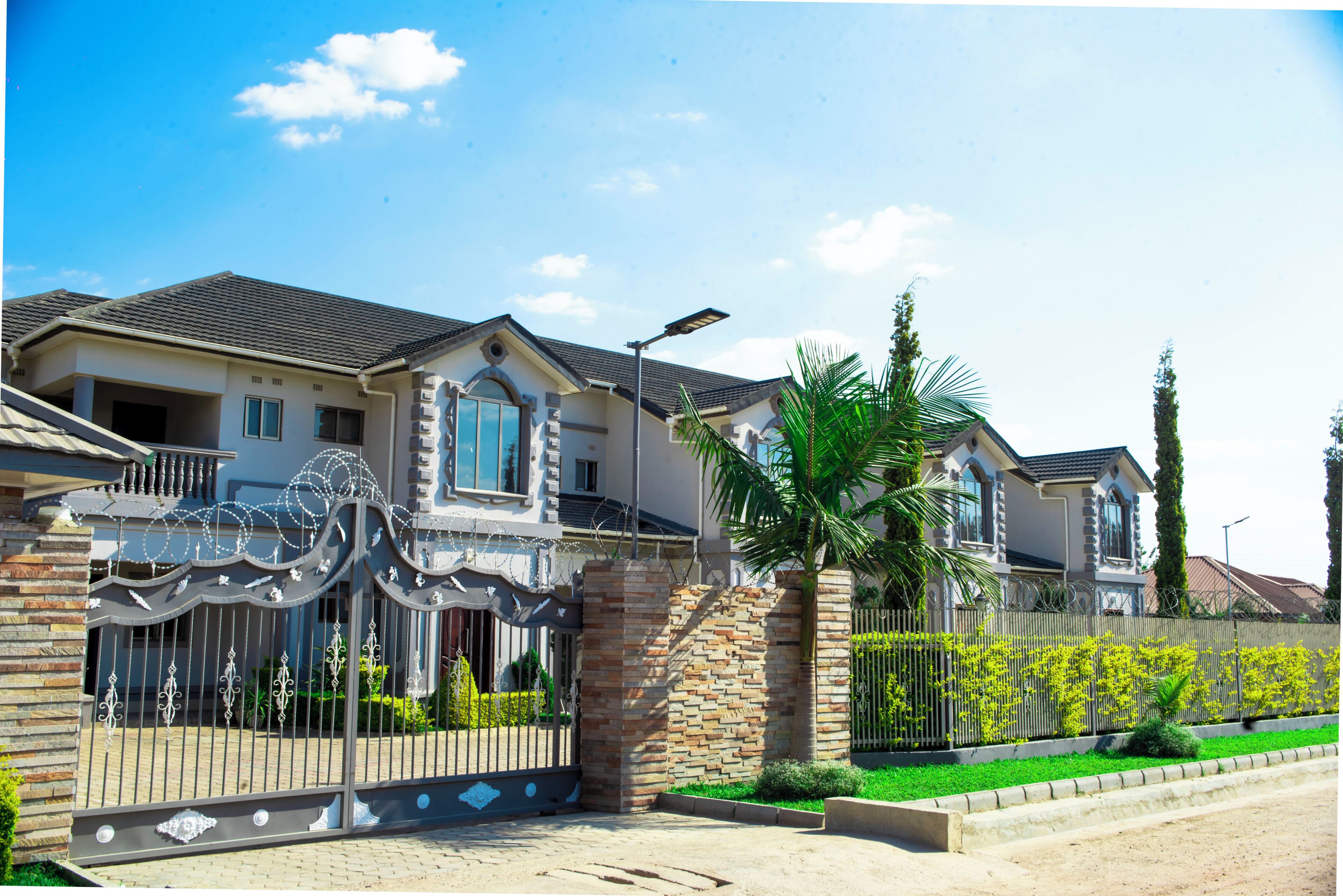 A two-story house with a gated entrance, a stone pillar, and a well-maintained lawn.