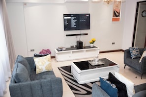 Ein modernes Wohnzimmer mit Flachbildfernseher, grauen Sofas, einem Couchtisch und einer weißen Unterhaltungsanlage.