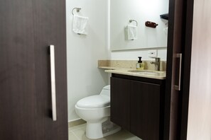 A modern bathroom with a white toilet, dark wooden cabinets, a beige countertop, and a mirror above the sink. - Apartasuite A 3 Min Del Aeropuerto Jmc (Rionegro)