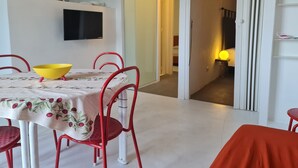 A dining area with a table set for two, a yellow bowl, and red chairs. A television is mounted on the wall above the table.