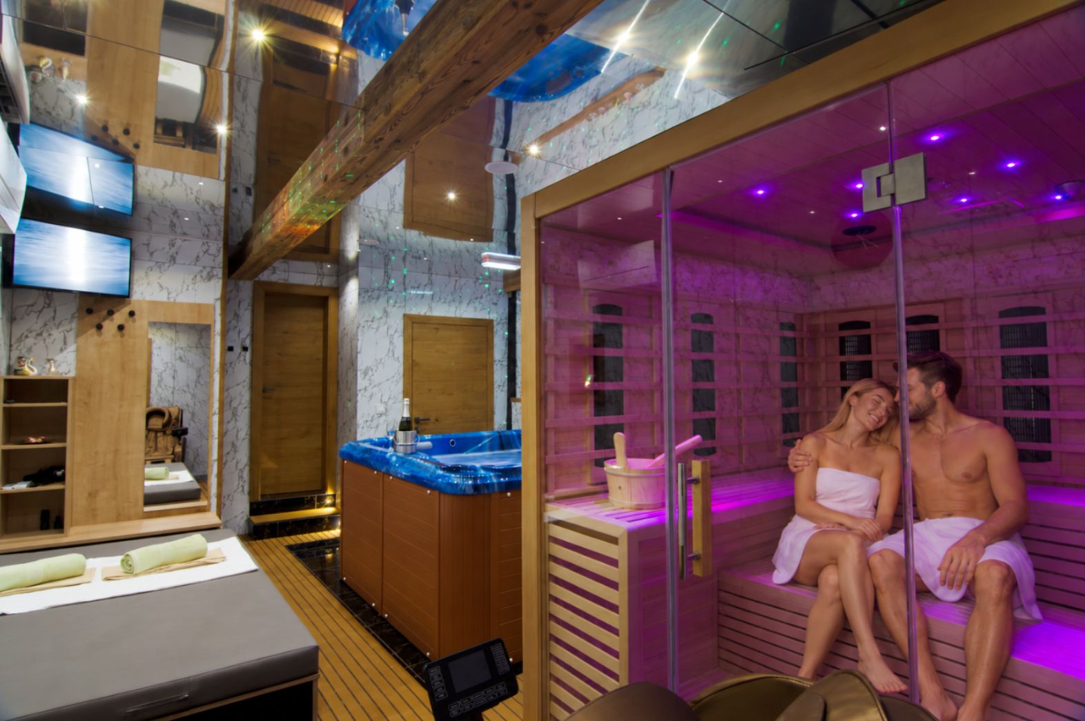 Une salle de sauna avec un banc en bois et une table de massage, un téléviseur et une armoire en bois sur laquelle se trouve une bouteille.