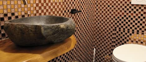 A bathroom with a stone basin, a toilet, and a sink with a faucet.