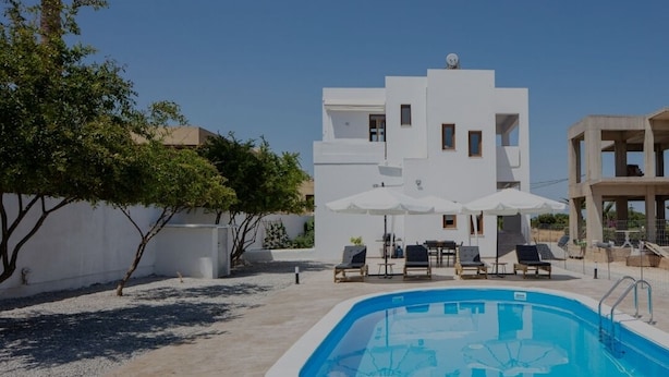 A modern white building with a swimming pool, outdoor seating, and a clear blue sky.